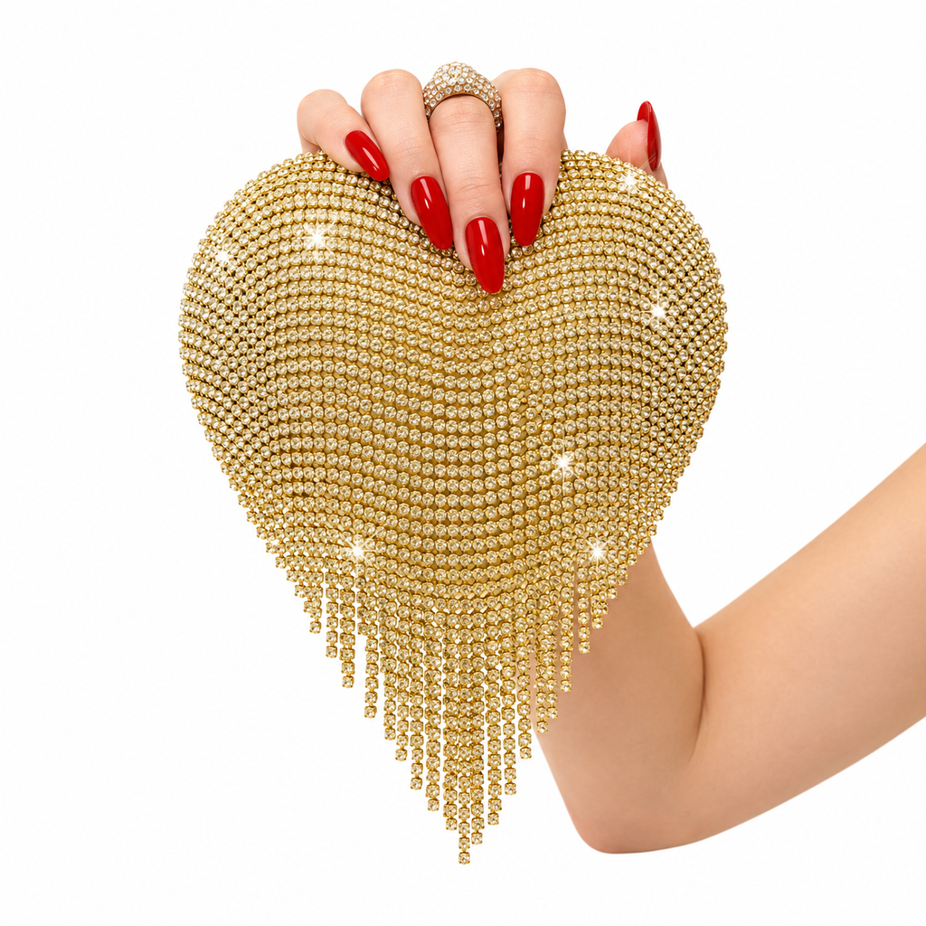 A gold rhinestone-embellished heart-shaped clutch purse with dangling fringe, held by a hand with red manicured nails against a plain white background.